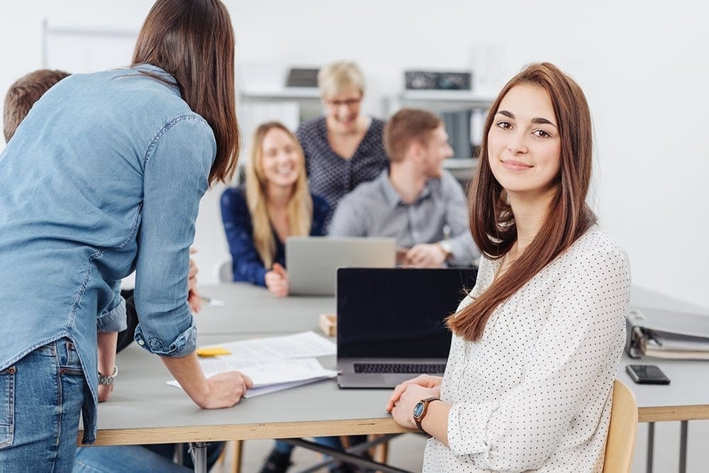 A smiling woman in a meeting with colleagues around a table