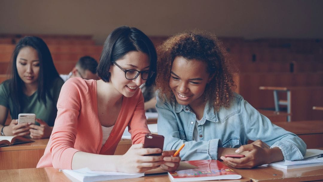 Two students smiling as they look at their results on a phone