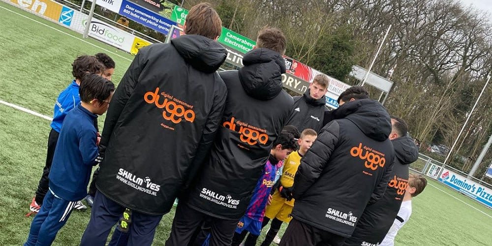 Young footballers and coaches in black Dugga and Skillmoves jackets on a pitch
